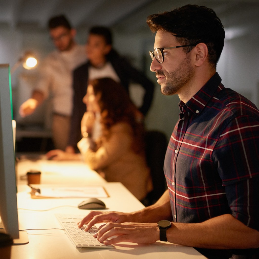 Professional working at a computer with colleagues in the background